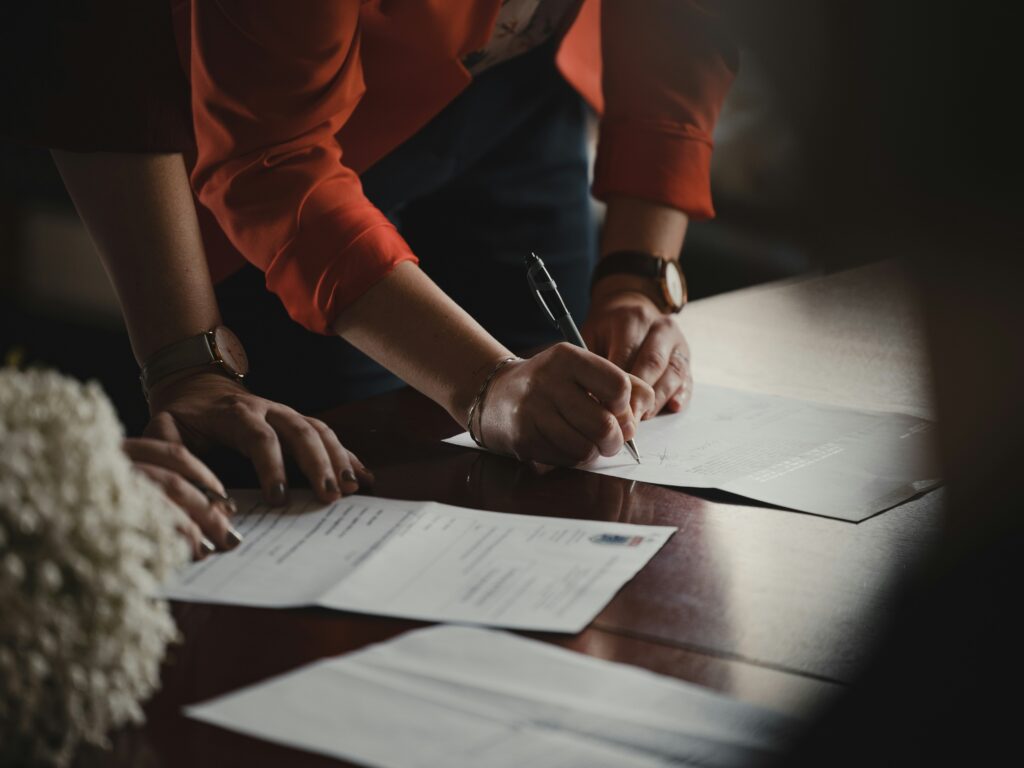 Person in an orange long-sleeve shirt writing on white paper while completing probate paperwork